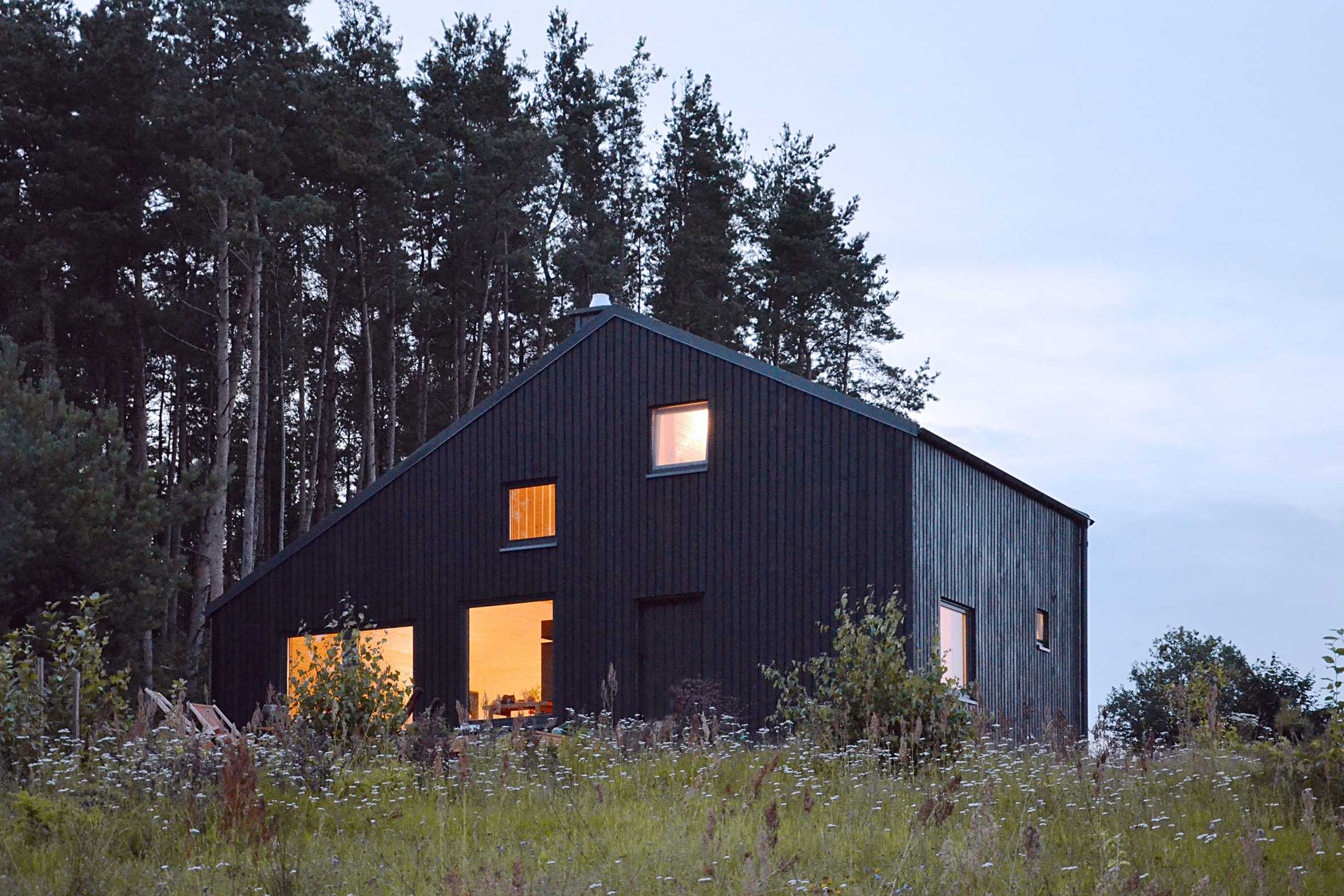 Black gabled house hewn from pine wood sits in the middle of a Polish forest-13
